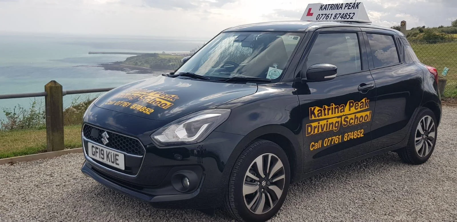 The Katrina Peak Driving School Suzuki Swift with the sea behind it