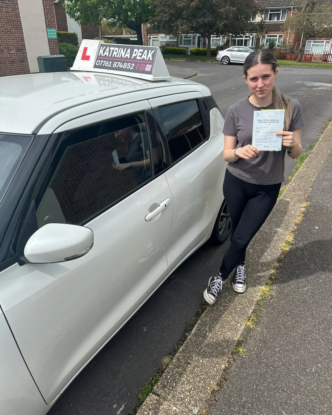 A newly qualified driver holding their pass certificate on a residential street in Kent