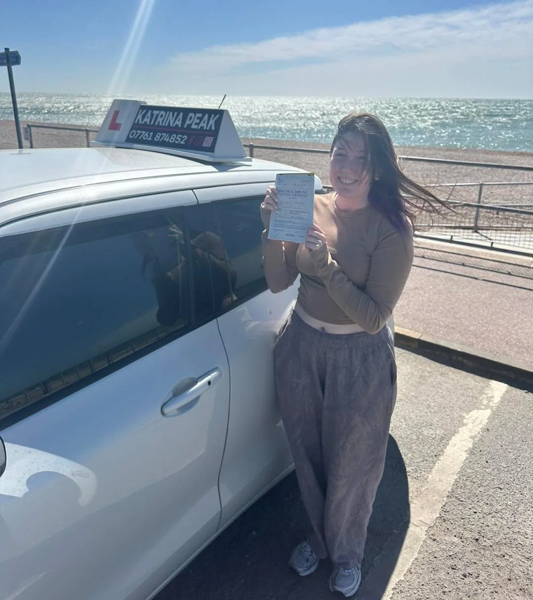 A pupil holding their pass certificate by the seafront in Hythe