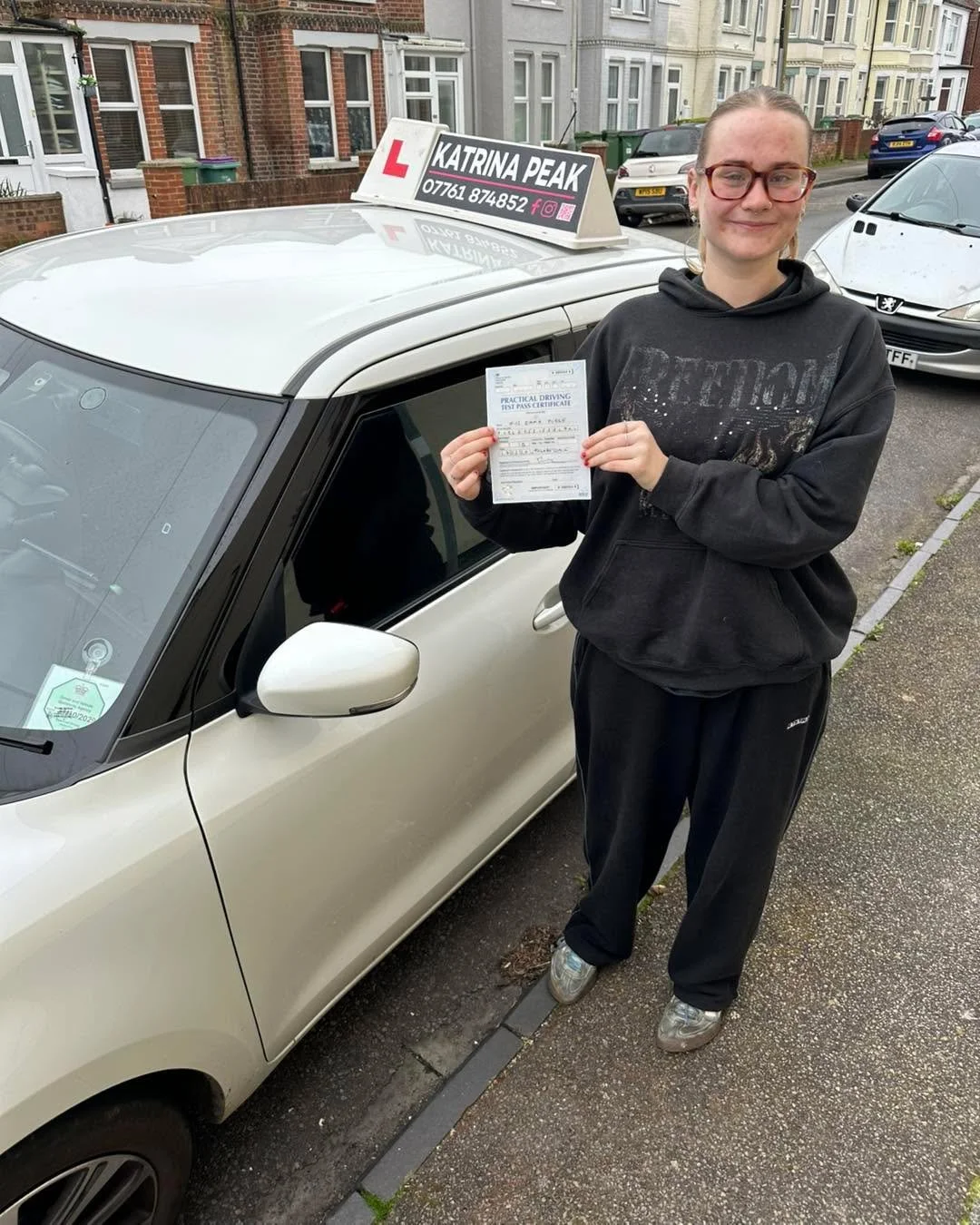 A pupil holding their pass certificate beside the learner car