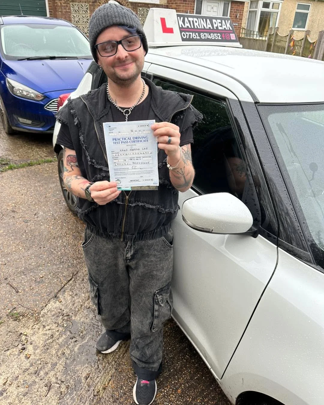 A pupil holding their driving test pass certificate beside the Katrina Peak Driving School car