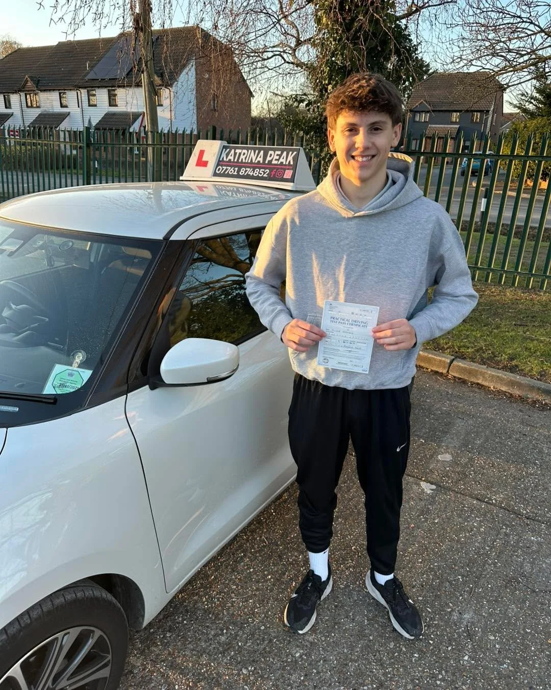 A pupil smiling with their pass certificate next to the Katrina Peak Driving School car