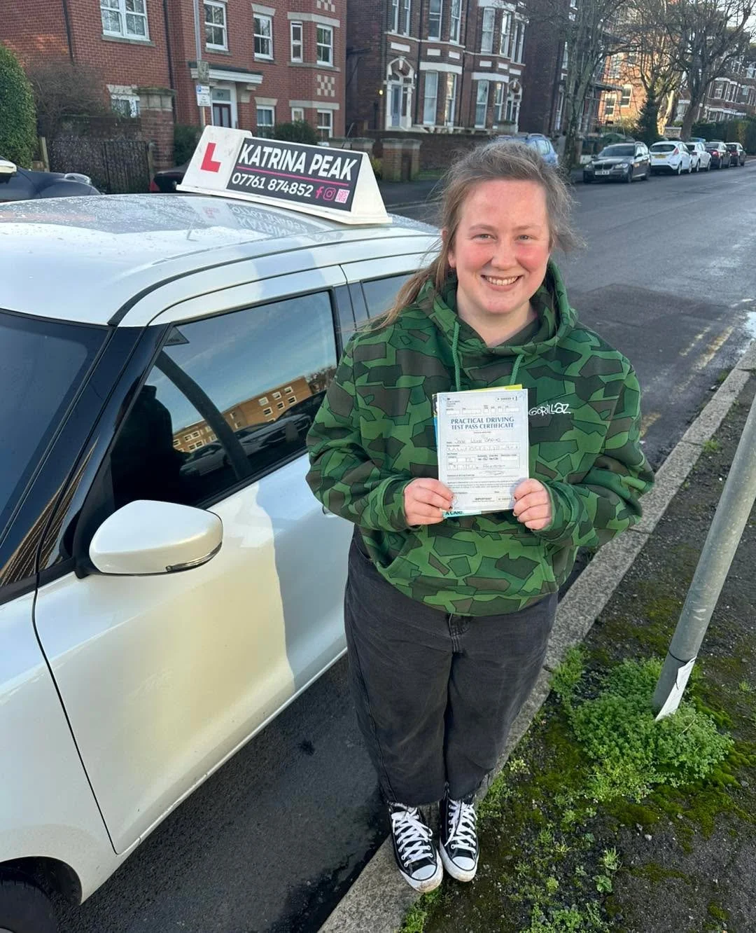 A pupil grinning with their driving test pass certificate beside the car
